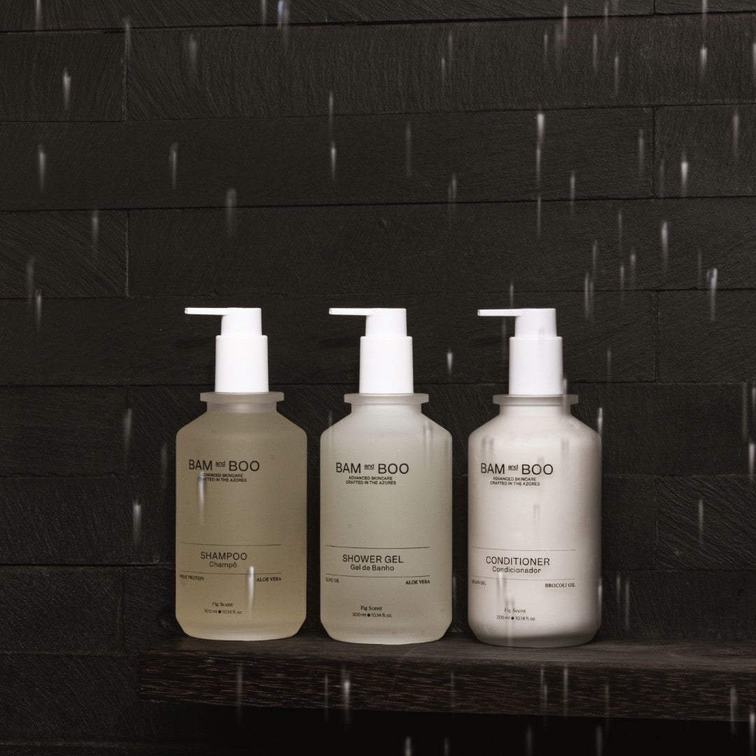 Three bottles of BAM and BOO skincare products on a dark wooden surface with a black tiled wall background. Natural Premium Hotel and Spa Amenities.