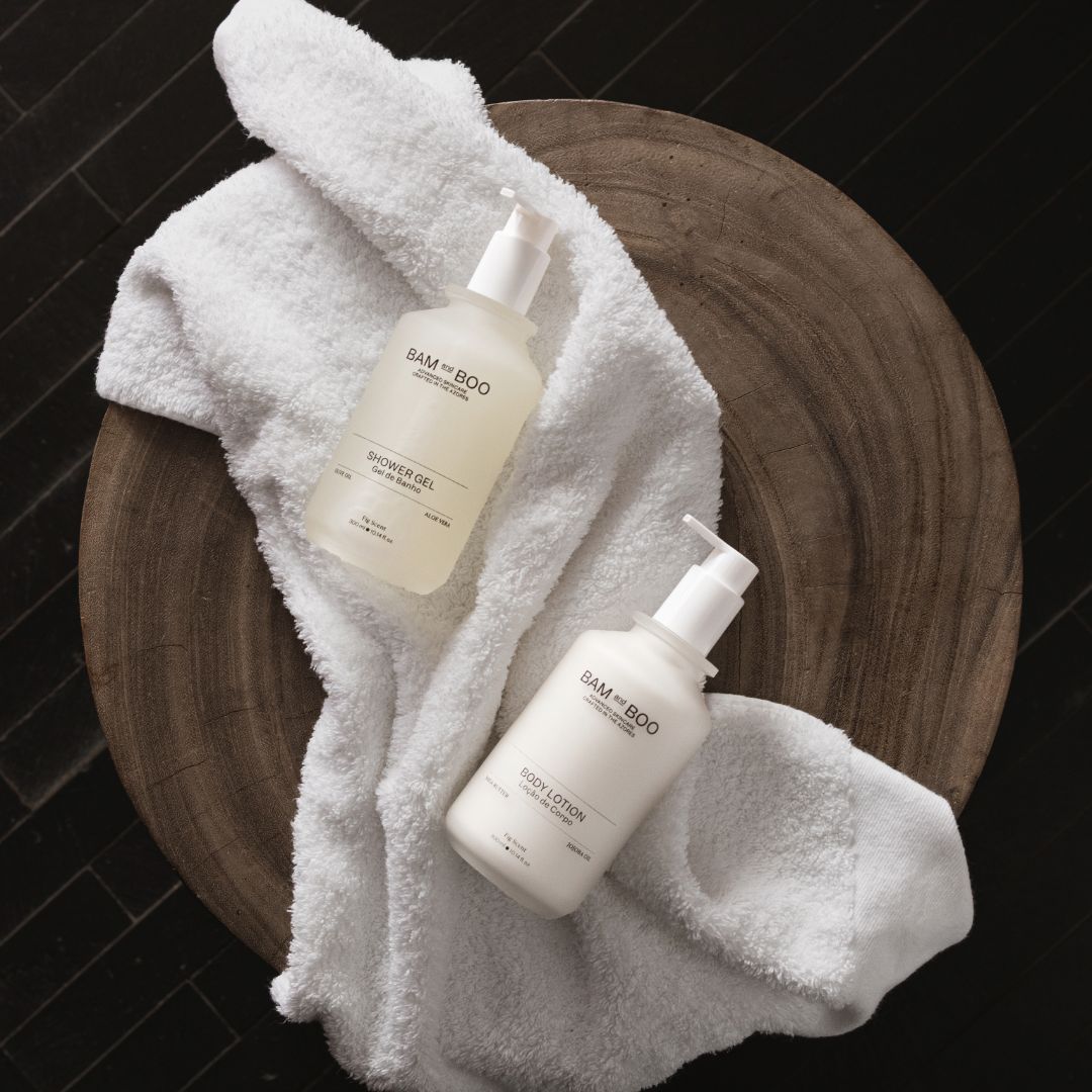 Two bottles of 'BAMBOO' skincare products on a white towel with a wooden background. Premium hotel amenities.